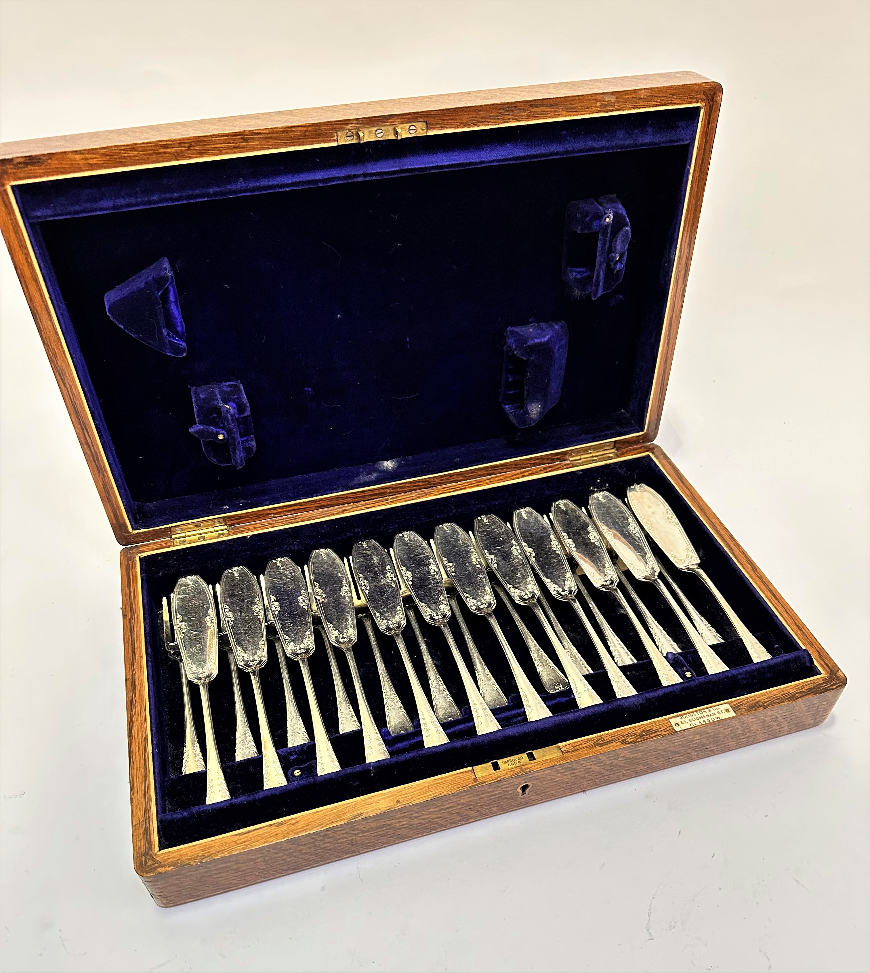 An Edwardian oak canteen containing twelve pairs of Epns engraved fish knives and forks, retained by