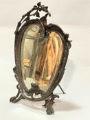 A cast metal Art Nouveau style table mirror with floral surmount and C scroll shaped bevelled