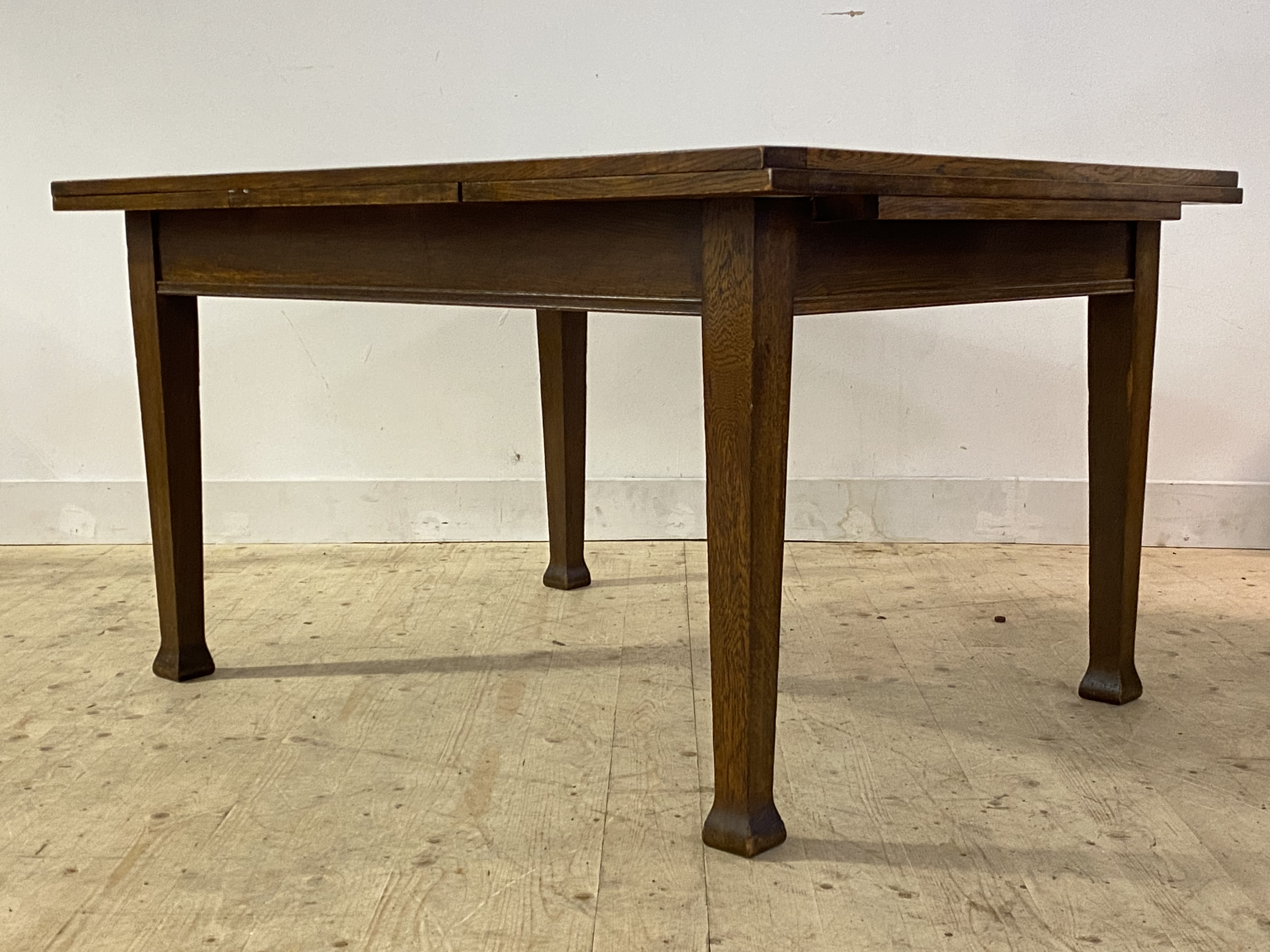 An oak Arts and Crafts duo drawer leaf dining table, the panelled rectangular top raised on square