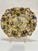 An Italian late 19thc Majolica scalloped dish decorated with Putti figures and ram enclosed within a