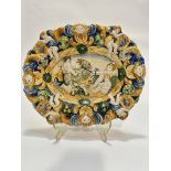 An Italian late 19thc Majolica scalloped dish decorated with Putti figures and ram enclosed within a