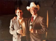 A photograph of Larry Hagman aka JR Ewing, posing with Marketing Gentleman with Bottles of Heineken,