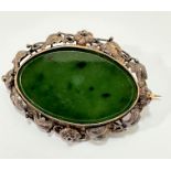 An Edwardian white metal and yellow metal mounted oval spinach green jadeite brooch with glass panel