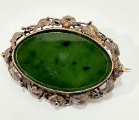An Edwardian white metal and yellow metal mounted oval spinach green jadeite brooch with glass panel