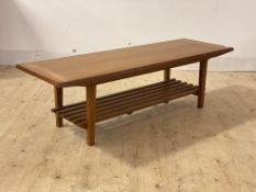 A mid century teak coffee table, with chamfered edge to top over slatted magazine rack, raised on