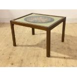 A mid century mahogany framed coffee table, the glass top with needlework panel behind, raised on