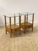 Ercol, A pair of blonde elm bedside tables, each with glass top over adjustable glass shelf and
