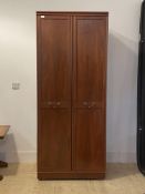 A two door cherry wood veneered wardrobe, twin panelled doors enclosing shelf and rail, moving on