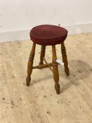 A vernacular varnished beech footstool, the circular upholstered top raised on turned supports