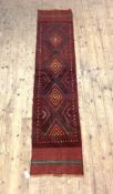 A Meshwani runner, hand knotted, the red ground with repeating lozenge design and bordered 257cm x