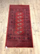 A Bokhara style red ground rug with six guls and bordered 180cm x 90cm