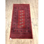 A Bokhara style red ground rug with six guls and bordered 180cm x 90cm
