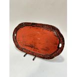 A Japanese red and black lacquered oval two handled tray with lily flower and leaf carved pattern to