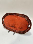 A Japanese red and black lacquered oval two handled tray with lily flower and leaf carved pattern to