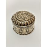 A Continental circular chased hinged box with fluted edge and embossed scene of figure with infant