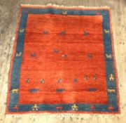 A Persian style Gabbeh rug, hand knotted, red ground with blue border having stylised animal