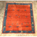 A Persian style Gabbeh rug, hand knotted, red ground with blue border having stylised animal