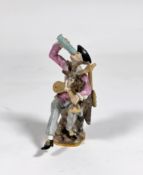 A Meissen style figure of a Harlequin drinking from a passglass and holding a goatskin bagpipe,