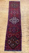 A Persian runner rug, hand knotted, the red field with five lozenge medallions and bordered 326cm