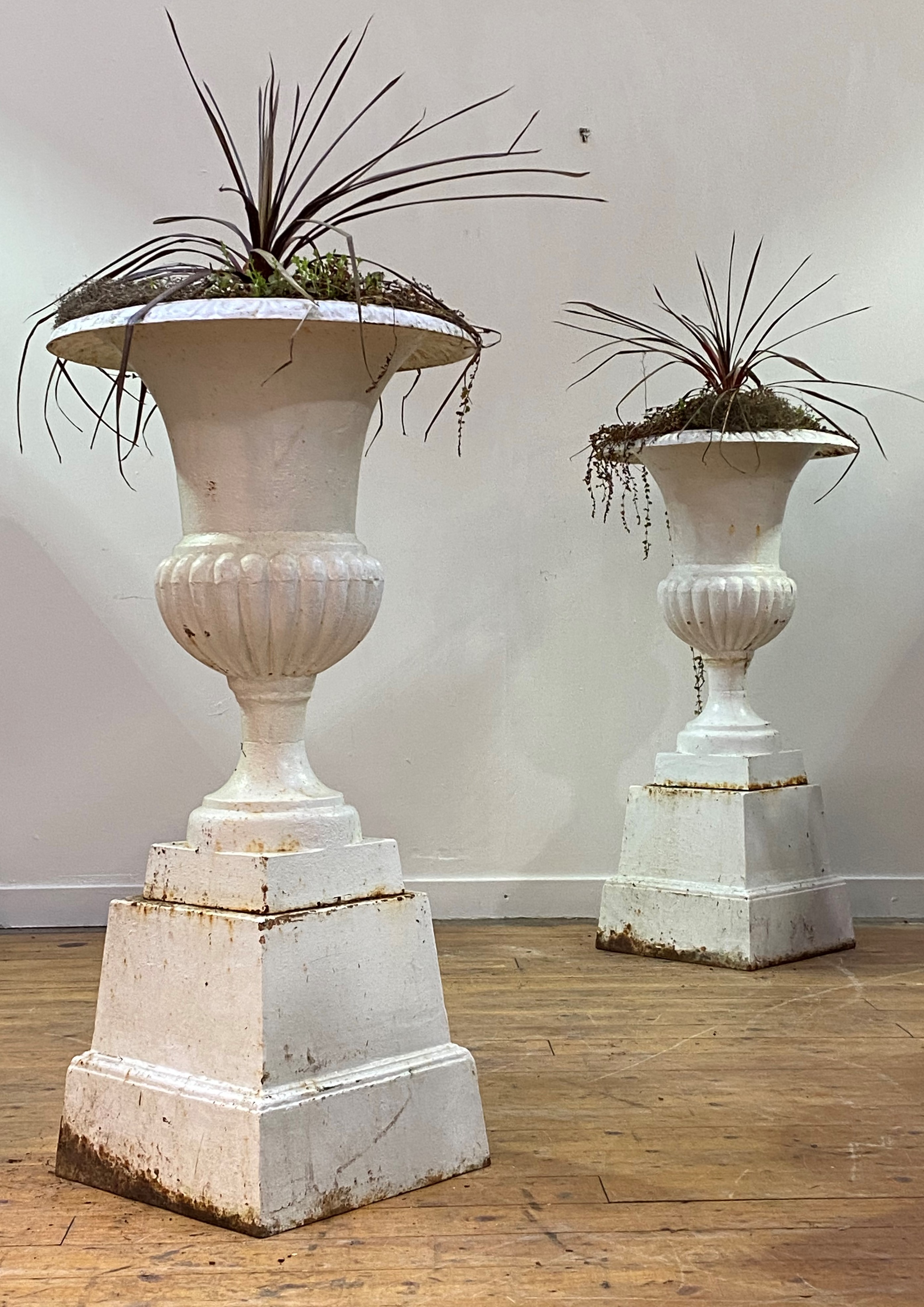 A pair of white-painted cast-iron garden urns on stands, the urns of campana form, on square section