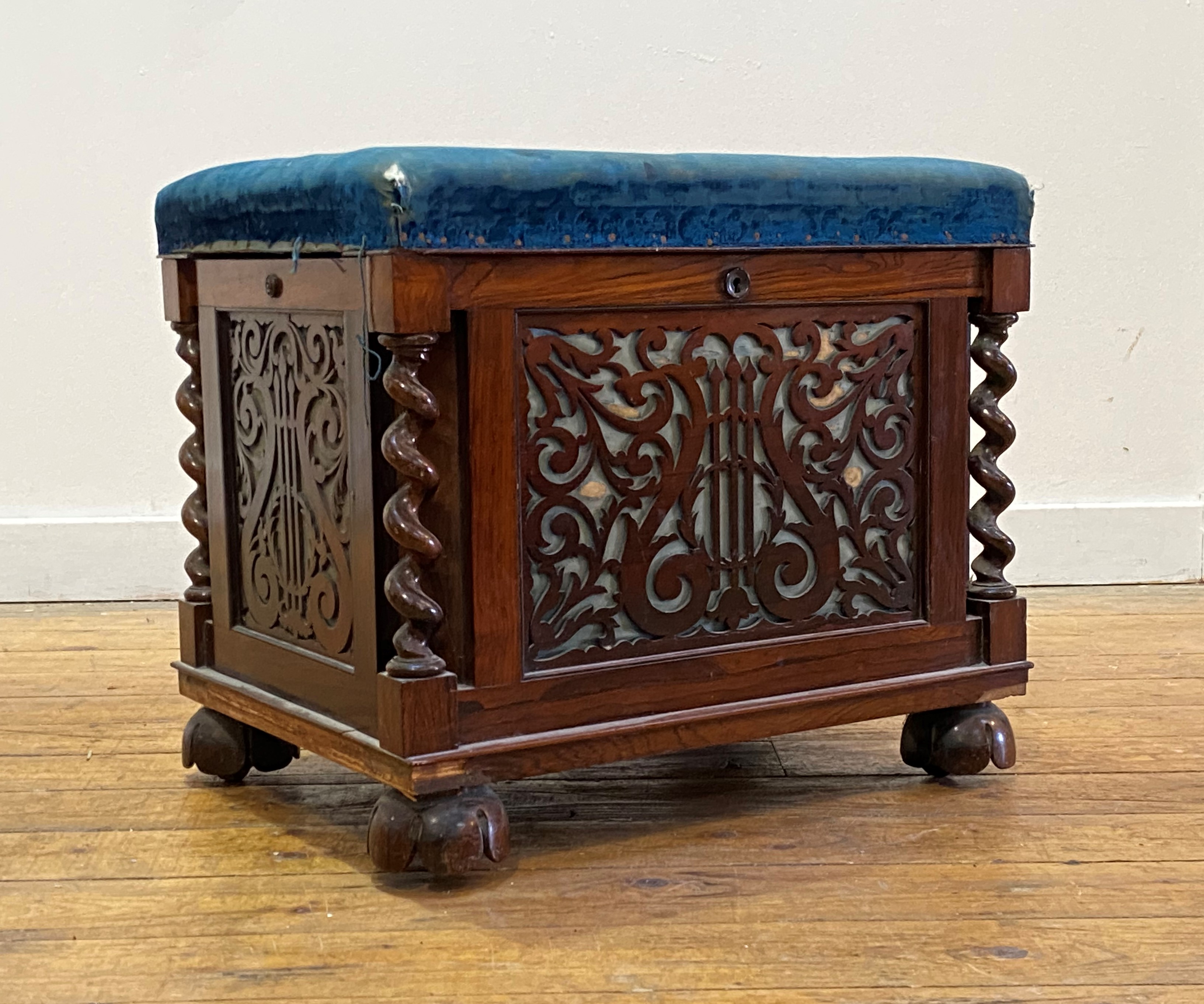 An early Victorian rosewood music stool, the worn blue velvet upholstered top lifting to an interior