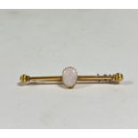 An opal-set yellow metal bar brooch, the oval-cut opal on a cylindrical bar with reeded ball