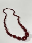 A long single graduated strand of "cherry" amber beads. Largest bead c. 28mm by 18mm, length of