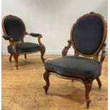 A pair of mid Victorian His and Hers walnut framed easy chairs, the oval back with floral carved