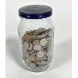 A jar containing a large collection of United Kingdom currency, including silver six pences, metal