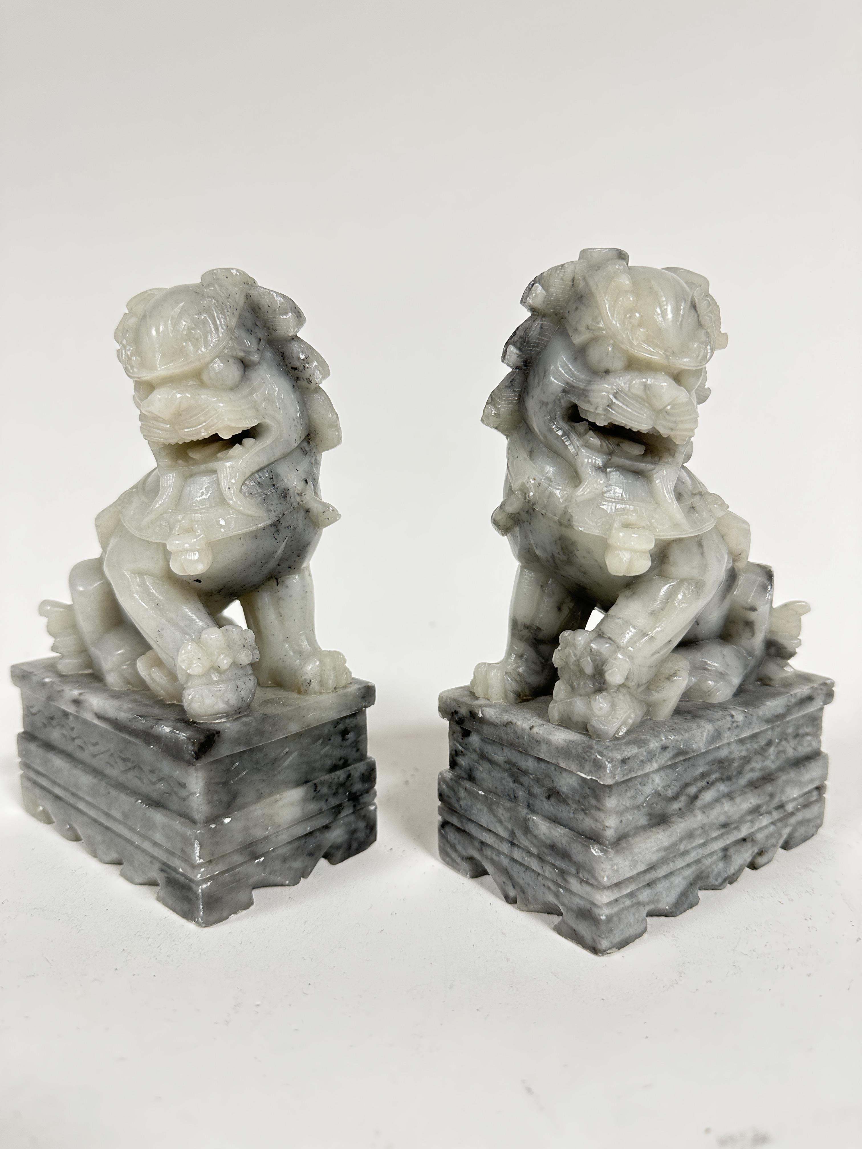 A pair of grey soapstone carved temple lions, raised on rectangular moulded bases, one with ball and