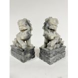 A pair of grey soapstone carved temple lions, raised on rectangular moulded bases, one with ball and