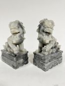 A pair of grey soapstone carved temple lions, raised on rectangular moulded bases, one with ball and