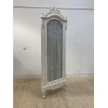 A French style white painted floor standing corner cabinet, with floral carved pediment over full