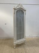 A French style white painted floor standing corner cabinet, with floral carved pediment over full