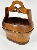 A Chinese elm water bucket of oval form with arched handle to top and carved stylised fruit and leaf