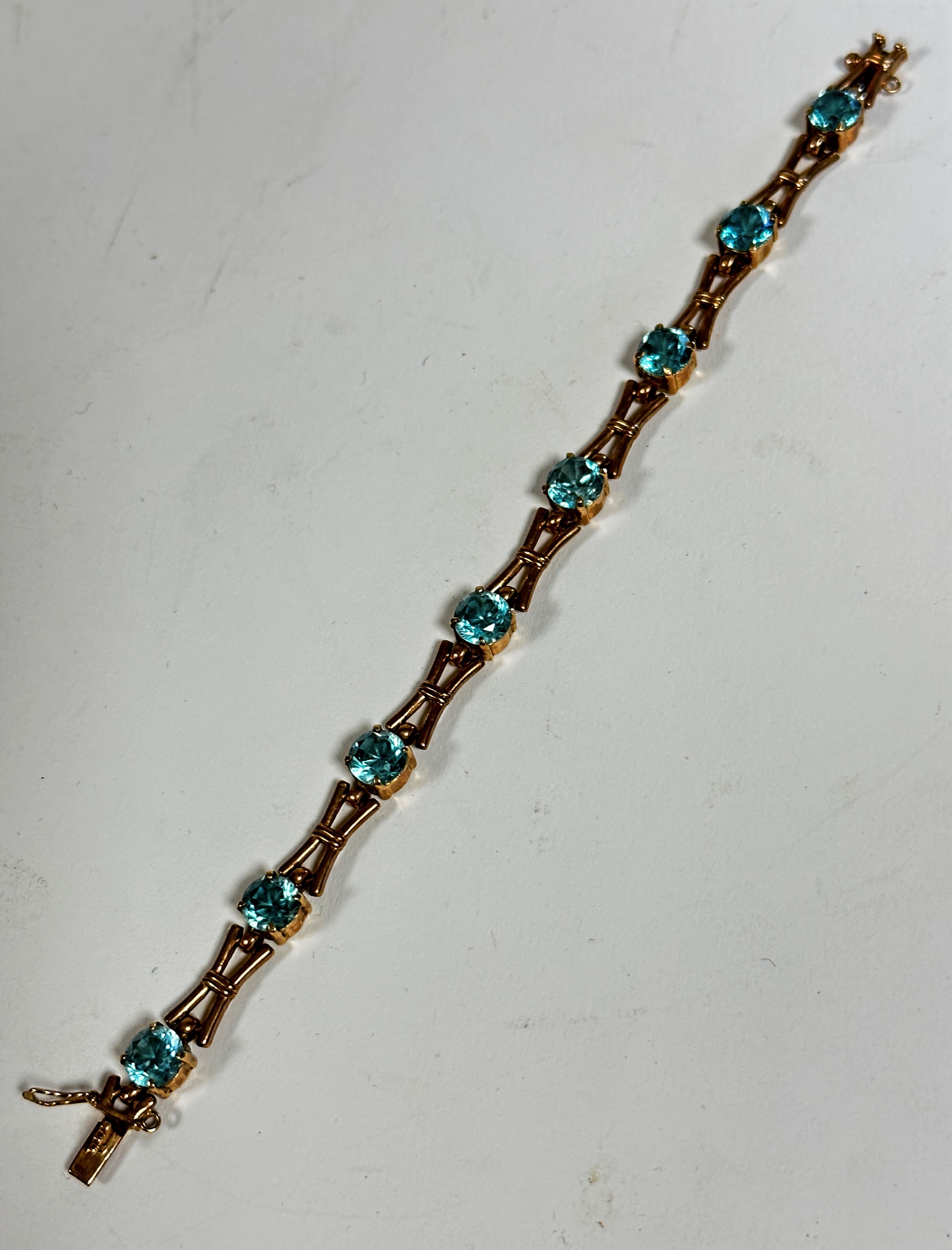 A 9ct gold link articulated line bracelet with X shaped links, set eight blue zircons in claw