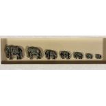 A box frame containing a Troop of Seven Graduated Elephants with gilded painted finish, glazed box