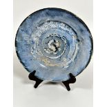 A pottery circular dish decorated with spiralling brown pale blue and turquoise blue glaze, with