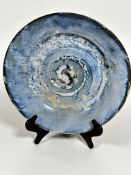 A pottery circular dish decorated with spiralling brown pale blue and turquoise blue glaze, with