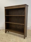 A 1930's oak open bookcase, floral carved frieze over two open shelves, raised on panel end