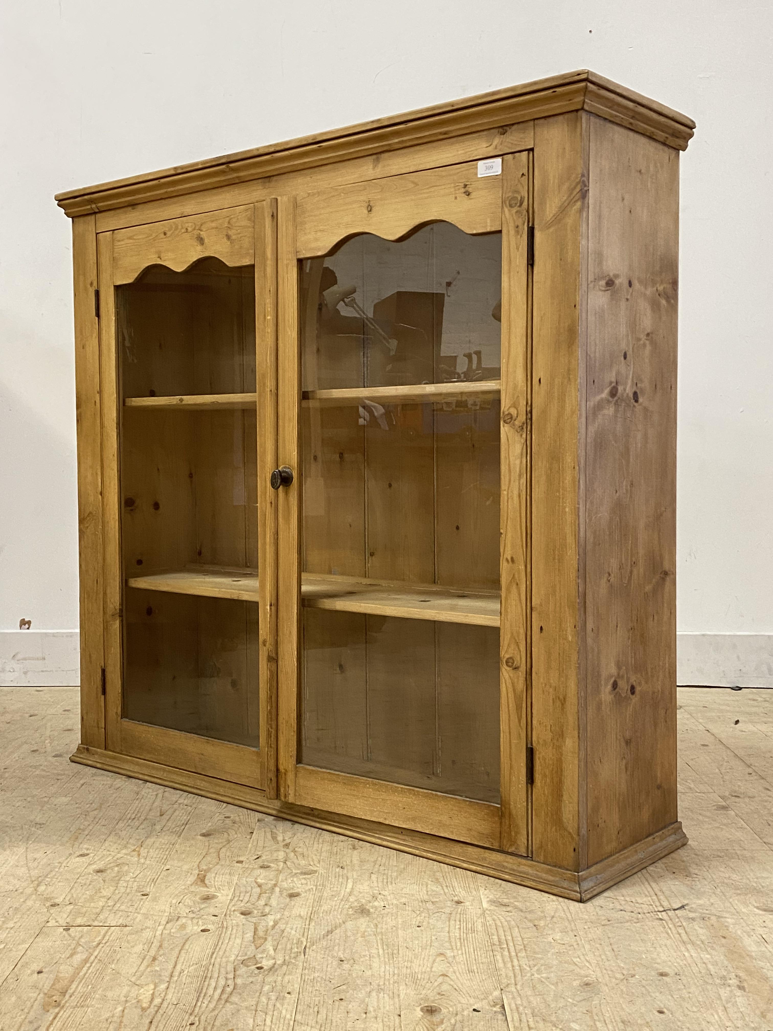 A late 19th/early 20th century pine two door glazed cabinet with two fixed shelves to interior,
