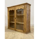 A late 19th/early 20th century pine two door glazed cabinet with two fixed shelves to interior,