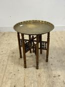 An Eastern style folding occasional table, the circular embossed brass tray top on turned