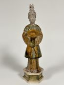 A reproduction Chinese pottery tomb figure of a courtier with headdress holding a bowl, with sage gr