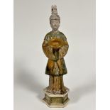 A reproduction Chinese pottery tomb figure of a courtier with headdress holding a bowl, with sage gr