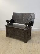 An early 20th century carved oak monks bench, the folding top over lion carved arm rests, hinged