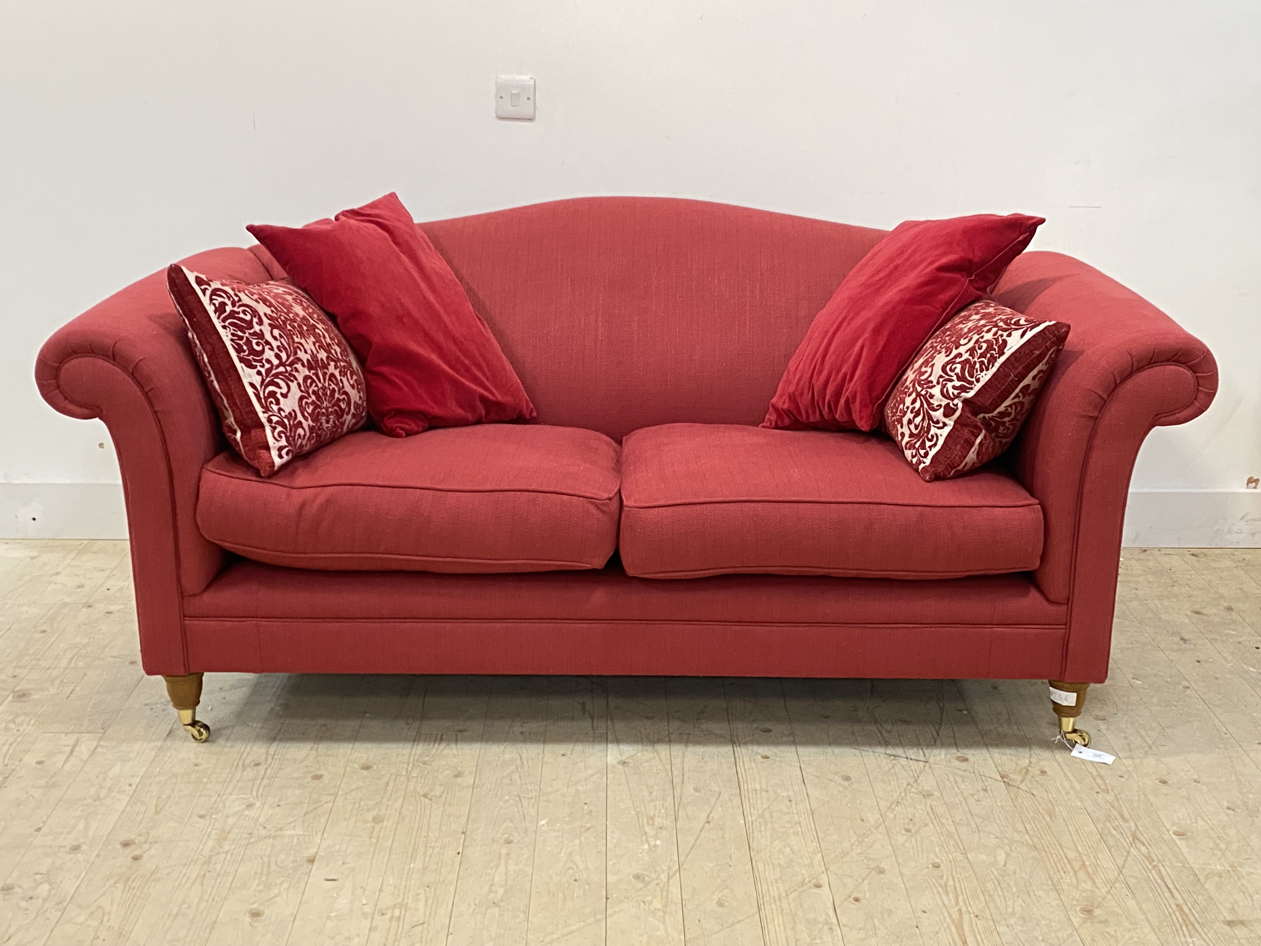 A traditional two seat sofa, upholstered in red herringbone fabric, raised on turned front