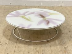 A contemporary circular low table, the floral patterned acrylic top over white metal supports,