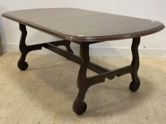 An oak extending dining table, the top drawing out to reveal magic leaf, raised on shaped scrolled
