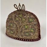 An Eastern burgundy padded wool crescent shaped tea cosy with gilt braided top with three loops